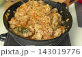 Stirring fried rice with chicken and mixed vegetables in cast iron skillet on stove 143019776