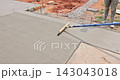 Worker uses long brush tool to smooth surface of wet concrete being poured at construction site. 143043018