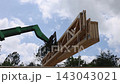 Workers are lifting large wooden trusses with telehandler at construction site is busy with activity. 143043021