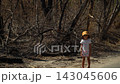 spring day, filming forest, remains burnt bushes trees, dried-up river background, natural disaster, absence animals birds, girl yellow Panama hat stands against backdrop burnt forest bored look 143045606
