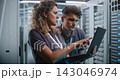 Female Engineer Using Laptop While Teammate Inspects Server Rack 143046974