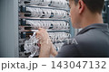 Male Network Technician Performing Physical Layer Cable Patching in Server Rack 143047132