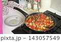 A woman mixes vegetables including zucchini and tomatoes in a pan. This cooking session captures the process of making zucchini caviar in a home kitchen. 143057549
