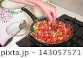 In the kitchen, a woman prepares zucchini caviar by chopping fresh vegetables like zucchini and tomatoes. She cooks them in a pan until soft, ready for serving. 143057571
