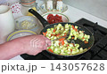 A woman is preparing zucchini caviar by salting fried zucchini mixed with onions and carrots. She stirs the ingredients in a pan. This takes place in a home kitchen. 143057628