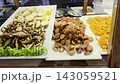 Selection of traditional Thai street food ingredients on white trays including sliced Chinese sausage, dried shrimp, and savory toppings displayed behind a glass counter at a local food stall. 143059521