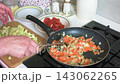 A woman is cooking zucchini caviar in her kitchen. She stews zucchini, tomatoes, peppers, onions and carrots, and then runs them through a meat grinder 143062265