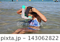 Young girl putting on snorkeling mask and breathing tube while sitting in shallow sea water during a sunny beach vacation 143062822