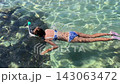 Young girl snorkeling above clear shallow water and rocky seabed, swimming forward in blue swimwear with pink fins in tropical sea 143063472