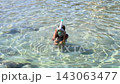 Young girl swimmer wearing snorkeling mask and tube moves through clear shallow seawater, viewed from above in a tropical coastal setting 143063477