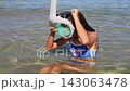 Young girl swimmer lifts full face snorkeling mask while standing in shallow clear water at a sunny beach 143063478