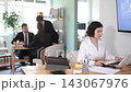 Woman employee of the bank office sits at the table and looks through documents and information on accounts on a laptop. Office worker typing on a laptop against the background of other workers 143067976