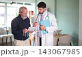 Male doctor and mature man patient examine papers, discuss medical tests result 143067985