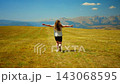 Young woman running freely across vast golden meadow with open arms, enjoying nature, mountain 143068595