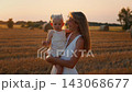 Smiling young mother holding her toddler daughter in a golden wheat field during warm sunset 143068677