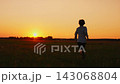 Young boy running across open grassy field at golden sunset, enjoying peaceful outdoor freedom, warm 143068804