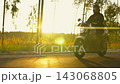Motorcyclist riding along a peaceful forest road at golden hour with bright sunlight flares 143068805