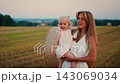 Young mother holding her toddler daughter in a sunlit harvested field with hay bales, sharing a 143069034