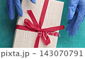 Pandemic present. Gift wrapping. Hands in protective gloves opening box untying red bow on blue textured background. 143070791
