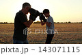 Father trains son in boxing drills with gloves across rural field. Parent and child practice punches with focus at sunset. Family fitness, mentorship and teamwork create sports footage. 143071115