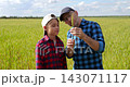 Father and boy examine wheat ear together in golden field while discussing crop quality. Child shows approval after learning farming skills. Family farm reflects agricultural expertise and successful  143071117