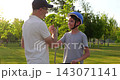 Dad helping child prepare for scooter ride in sunny park. Parent and kid shake hands after safety guidance, representing trust, encouragement, family care, active childhood and outdoor recreation 143071141