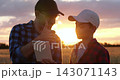 Farmer dad teaches son about wheat crops using tablet in field at sunset. Boy holds wheat ears while father explains field data, combining family bonding, agricultural education, technology, tradition 143071143