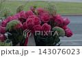 Bright pink rose bouquet with delicate white filler flowers beside calm water in soft outdoor light 143076023