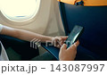 Unrecognizable traveler shopping online with smartphone during airplane flight. Hands browsing ecommerce products on mobile device. Digital consumer behavior and travel technology concept 143087997