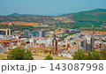 Spanish Mediterranean cityscape with dense urban rooftops and historic church architecture. Colorful residential buildings beneath green hills. Panoramic urban landscape in sunny Spain under clear 143087998