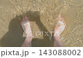 Warm ocean water rippling around barefoot man at sandy shoreline. Sunlight sparkling across clear shallow waves. Beach holiday, coastal leisure and refreshing summer escape 143088002