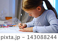 First grade girl writes with pencil while studying at home. Focused child develops handwriting and learning skills with selective focus and shallow depth of field 143088244