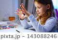 First grade girl stretches tired fingers during handwriting practice at home. Child takes a break from writing to relieve hand fatigue with selective focus 143088246