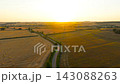Silver crossover driving along winding country lane through harvested farmland at golden hour. Aerial view of road travel between fields and hay bales. Countryside journey across rural landscape in 143088263