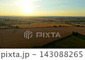 Expansive cropland under low sunset with hay bales and long tree shadows across rural fields. Harvest season landscape in warm golden light. Grain production, agricultural revenue and profitable farm 143088265