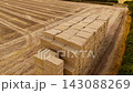 Stacked straw bales in harvested agricultural field after cereal crop season. Large rectangular hay bale storage for livestock farming and animal feed. Rural agribusiness landscape with dry farmland 143088269