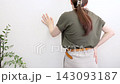 A woman's back as she leans against a wall, enduring back pain. 143093187