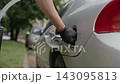 Person wearing protective black gloves refueling silver car empty tank with gasoline from shiny metal jerry can, concept of roadside emergency, fuel crisis, close-up, slow motion. 143095813