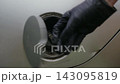 Close-up of hand in black glove opening car fuel door. Person unscrewing and removing gas cap, preparing vehicle for refueling. Concept of roadside assistance, fuel crisis. Shooting in slow motion. 143095819