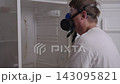 Professional cleaning service worker wearing respirator mask and safety goggles inspects inside of filthy, empty refrigerator, man turns head to looking at camera with smile. Shooting in slow motion. 143095821