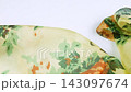 Green and yellow floral silk fabric gently falls onto a clean white background in slow motion. This elegant textile texture is perfect for commercial fashion advertising and luxury beauty branding. 143097674