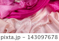 Smoothly falling vibrant pink silk fabric drops onto a soft peach textile creating elegant folds. This slow motion movement showcases the premium quality of the luxurious contrasting drapery.  143097678