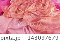 Premium peach silk fabric gently falls onto luxurious orange and pink scarfs in slow motion. This elegant drape showcases the smooth texture of high-quality pastel textiles.  143097679