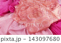 Pink and peach patterned silk fabric gently falls onto a pile of matching pink, magenta, and rose textiles. This slow motion sequence captures the smooth movement and elegant folds of the material. 143097680