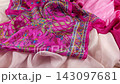Pink silk shawl with a traditional paisley pattern falls in slow motion onto layered luxury fabrics. This vibrant fuchsia and emerald green textile beautifully demonstrates the soft texture. 143097681
