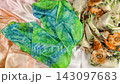 Bright green tie-dye silk fabric falls gently in slow motion onto elegant collection of colorful scarves. The smooth handcrafted textile creates soft luxurious folds over the lying background cloths 143097683
