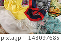 Slow motion top view of colorful silk fabrics and scarves gently falling onto each other. Bright yellow, red, and patterned textiles create a vibrant and dynamic layered composition.  143097685