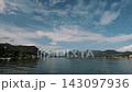 Panoramic view of calm water framed by green hills and distant mountains on sunny day 143097936
