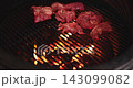 A man puts pieces of raw meat on the grill of a round grill, hot coals under the grill, and an egg-shaped grill. 143099082