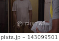 Young delivery man receiving take away food order in plastic bag from delivery person at home entrance. Concept of convenience of meal delivery services in apartment setting, close-up, slow motion.. 143099501